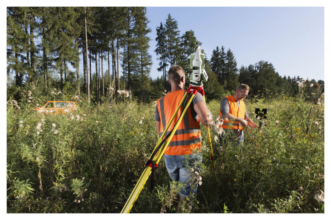 Arbeiten im Außendienst zwei Mitarbeiter des Vermessungsamts stehen im hohen Gras auf einer Lichtung im Wald